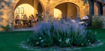 Lavender plant in the park of the ancient Monastero San Silvestro Farmhouse.
									In the background, some people are having dinner together, sheltered from the porch of the monastery
